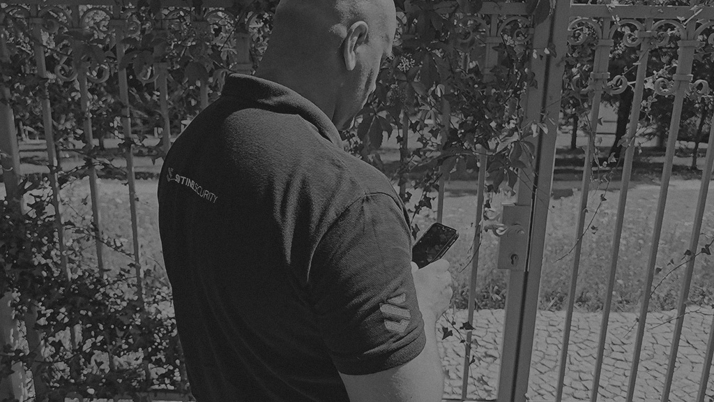 A Sentinel Security officer confirming a perimeter checkpoint from a phone at a gate.